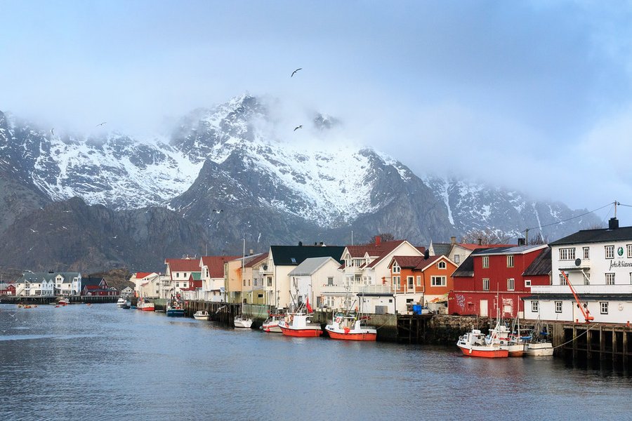 Fargerike hus og fiskebåter i Henningsvær i Lofoten med snødekte fjell
